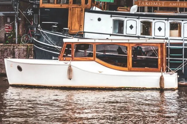 Barcă de lemn legată la mal, pe un canal îngust, cu stuf auriu de ambele părți